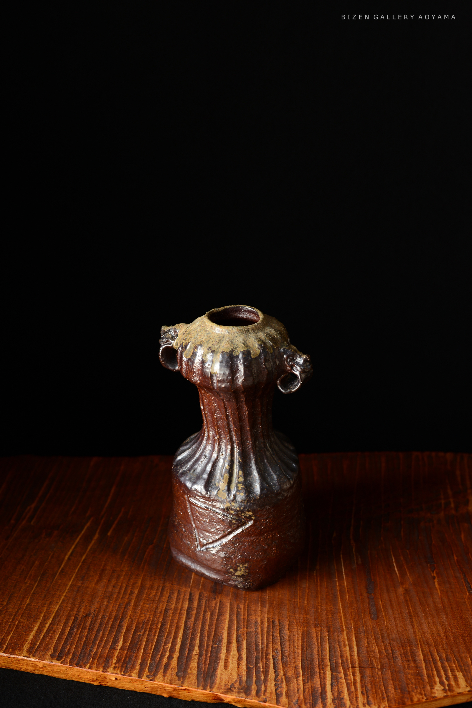 黒い背景に置かれた独特な形状の土器。上部はリブ状になっており、側面には装飾的な模様が施されている。木製のテーブルの上に立てられている。