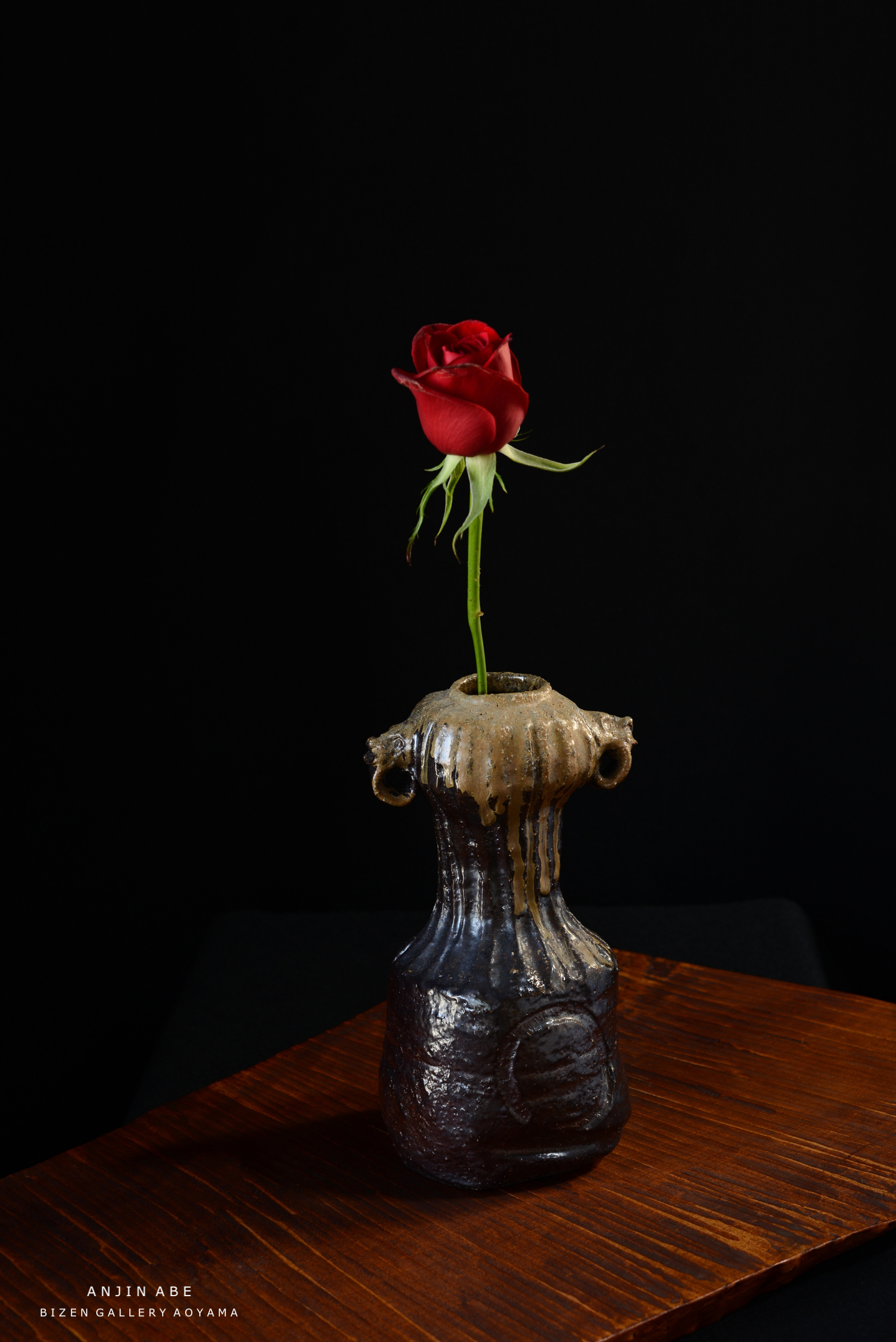 黒い背景に赤いバラが飾られた陶器の花瓶。