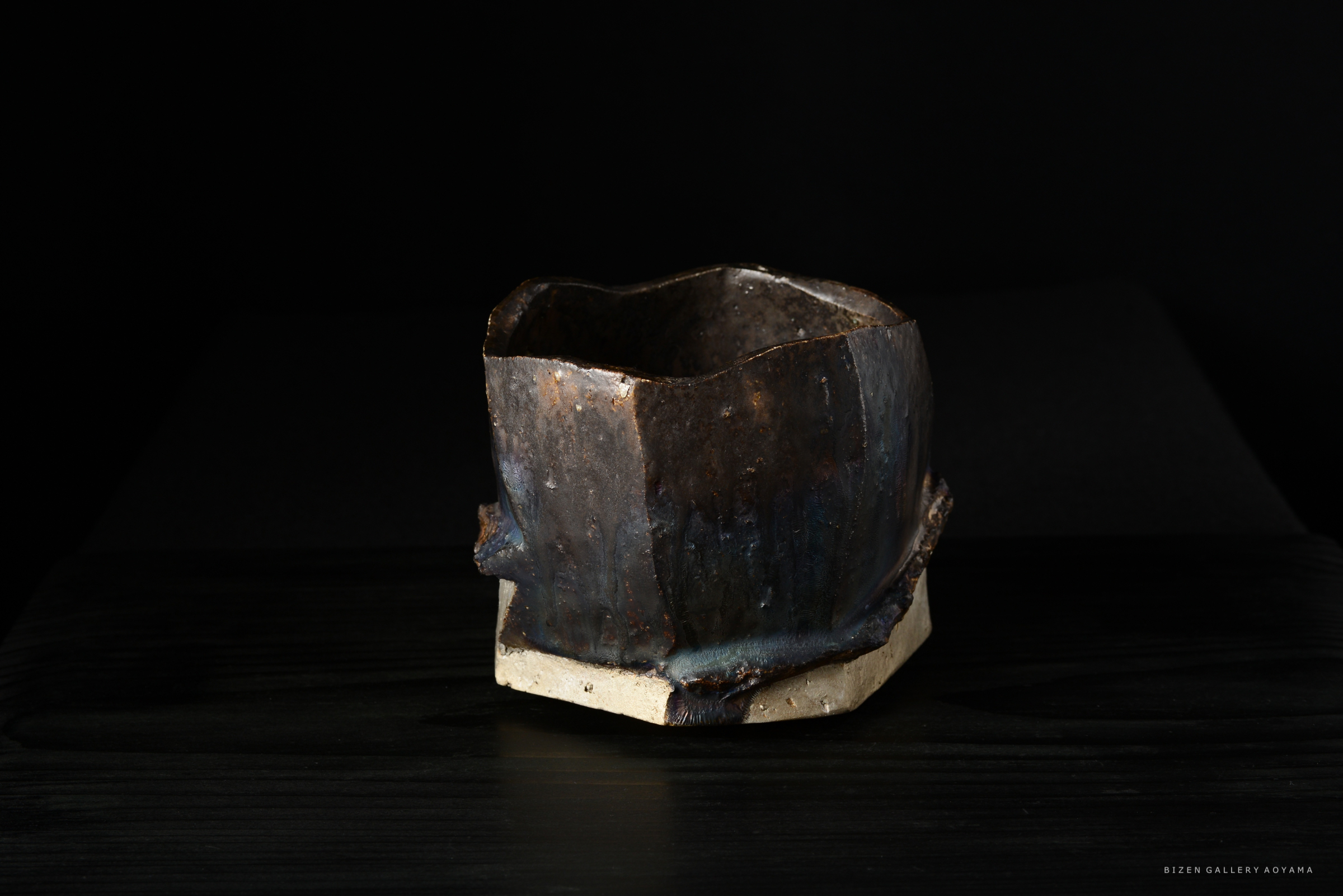 黒い背景に置かれた独特な形状の陶器。下部は白く、上部はさまざまな色合いの釉薬が施されている。