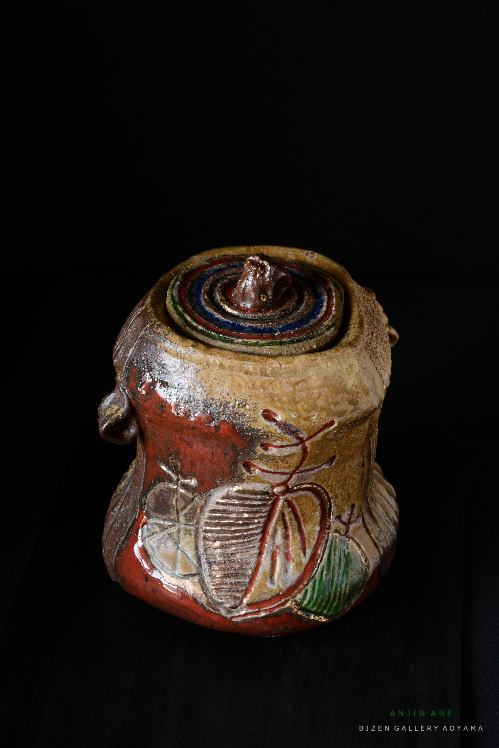 色とりどりの縞模様の蓋が特徴的な陶器の壺、造形物の表面には装飾的な絵柄が施されている。