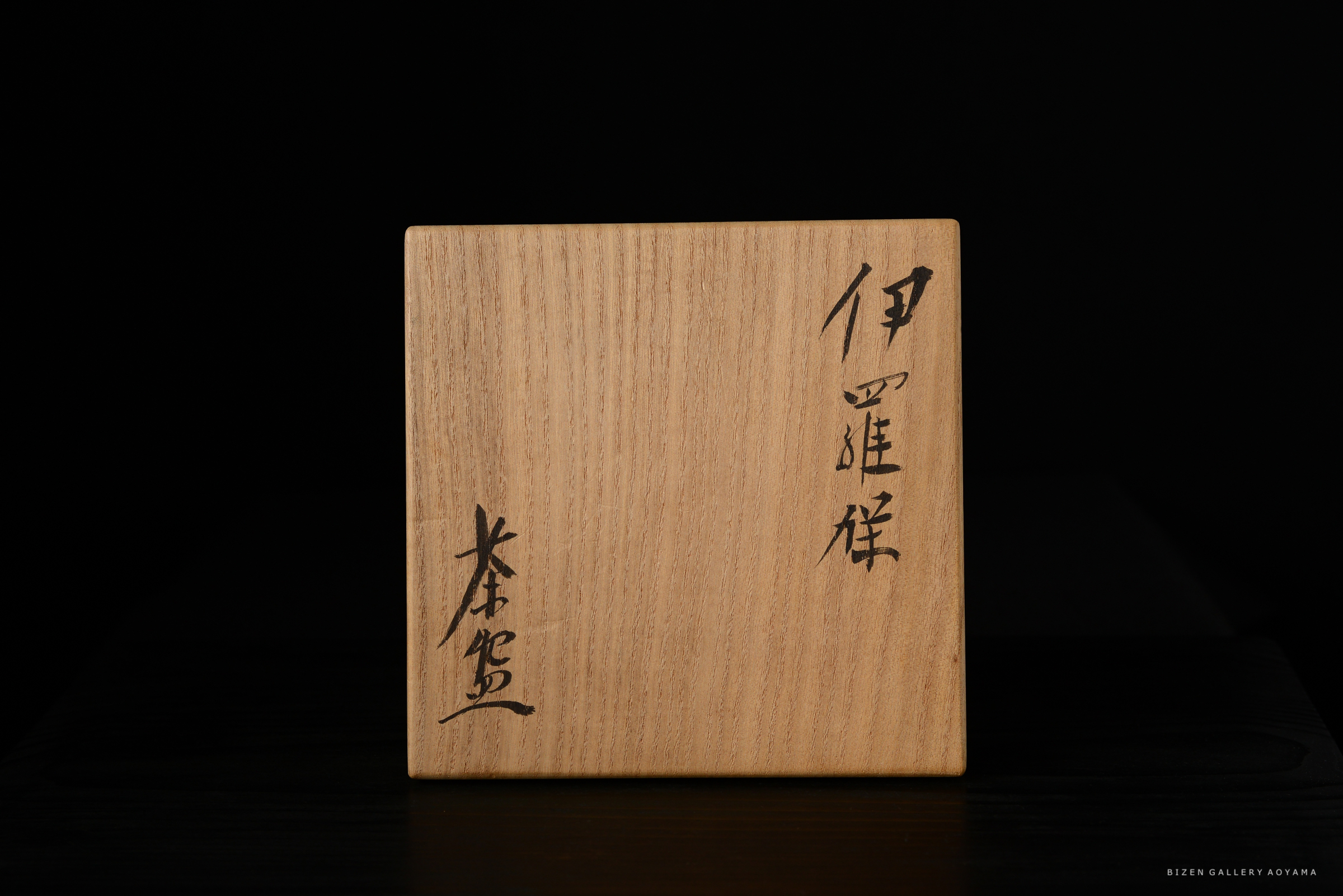 木製の箱の側面に書かれた日本の漢字が見える。背景は黒。
