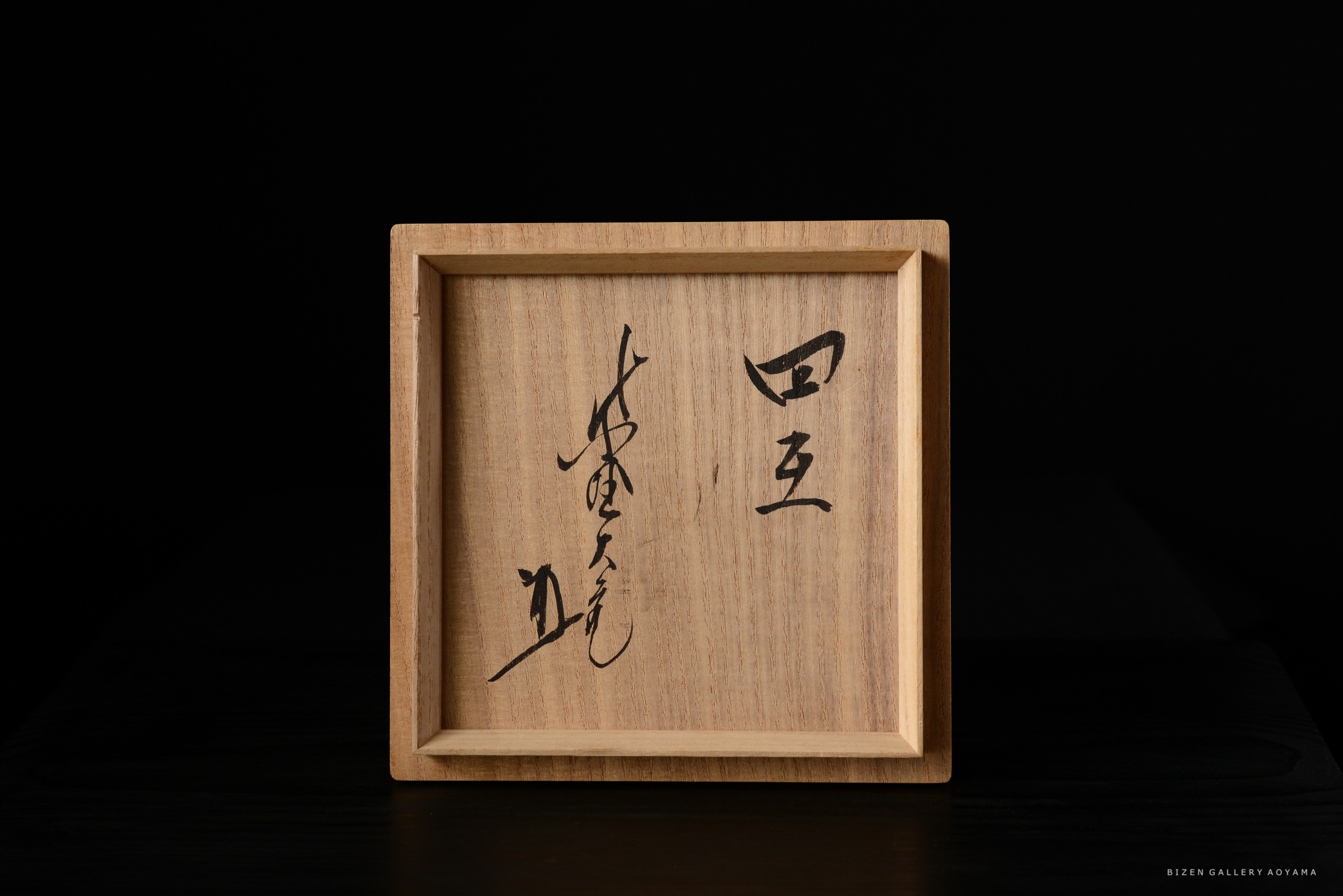 木製の箱の前面に書かれた漢字と文字が見える。背景は黒色。