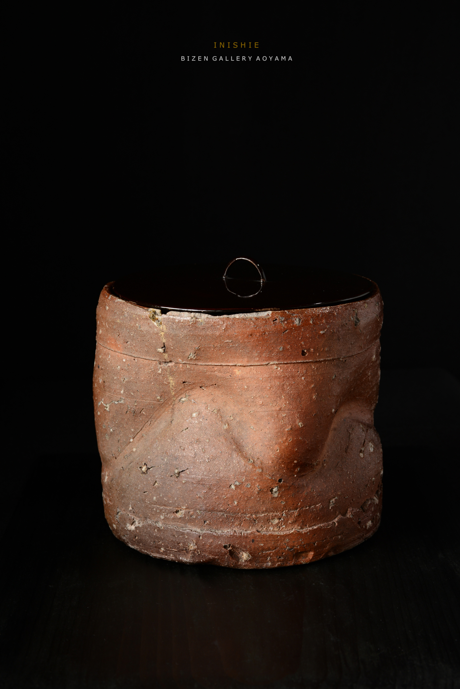 黒い背景の上に置かれた陶器のふた付き容器。表面は自然な土の質感で、独特の形状を持っている。