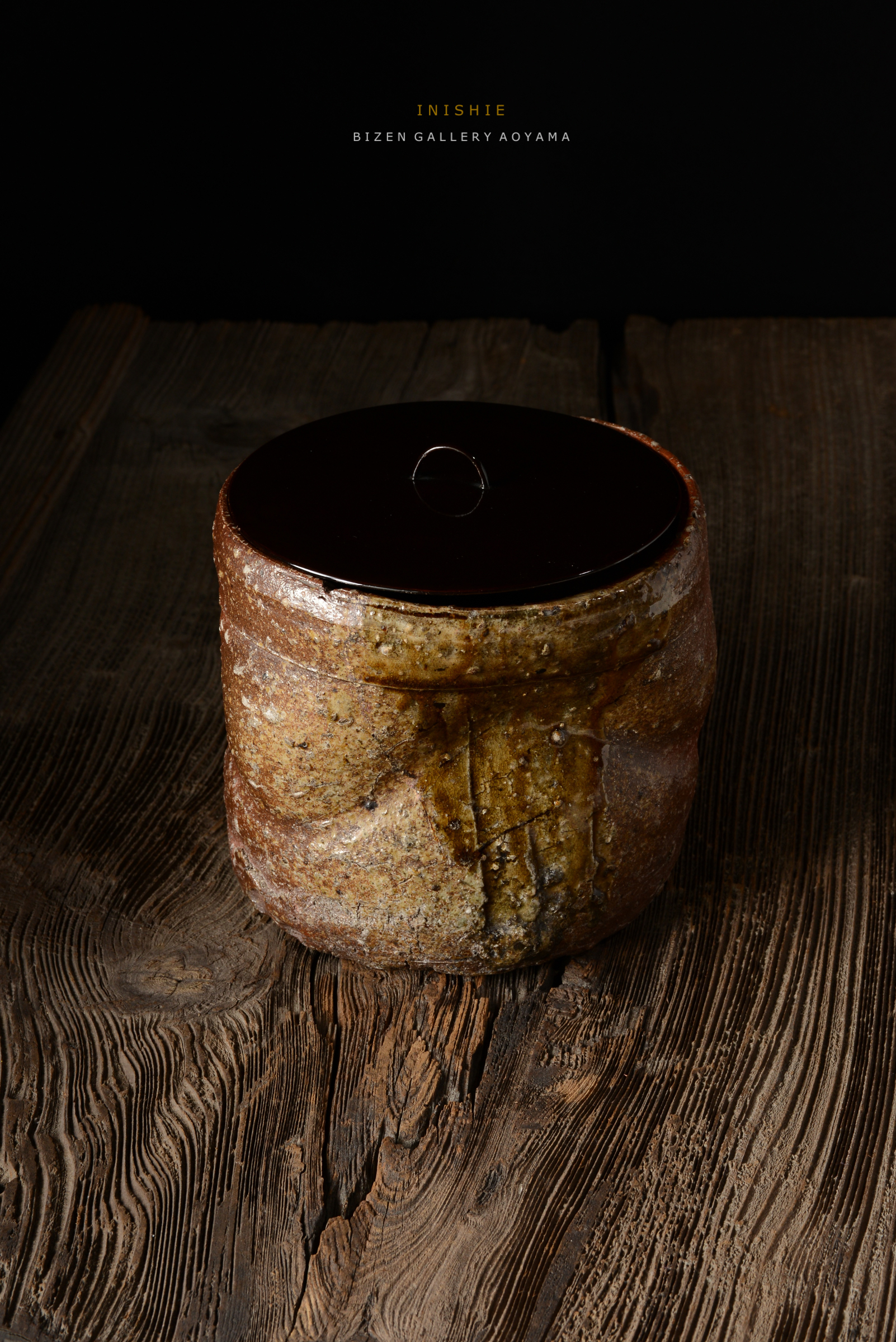 木のテーブルの上に置かれた陶器の壺。上部は光沢のある黒い蓋が載っていて、側面は自然な色合いと質感を持つ。