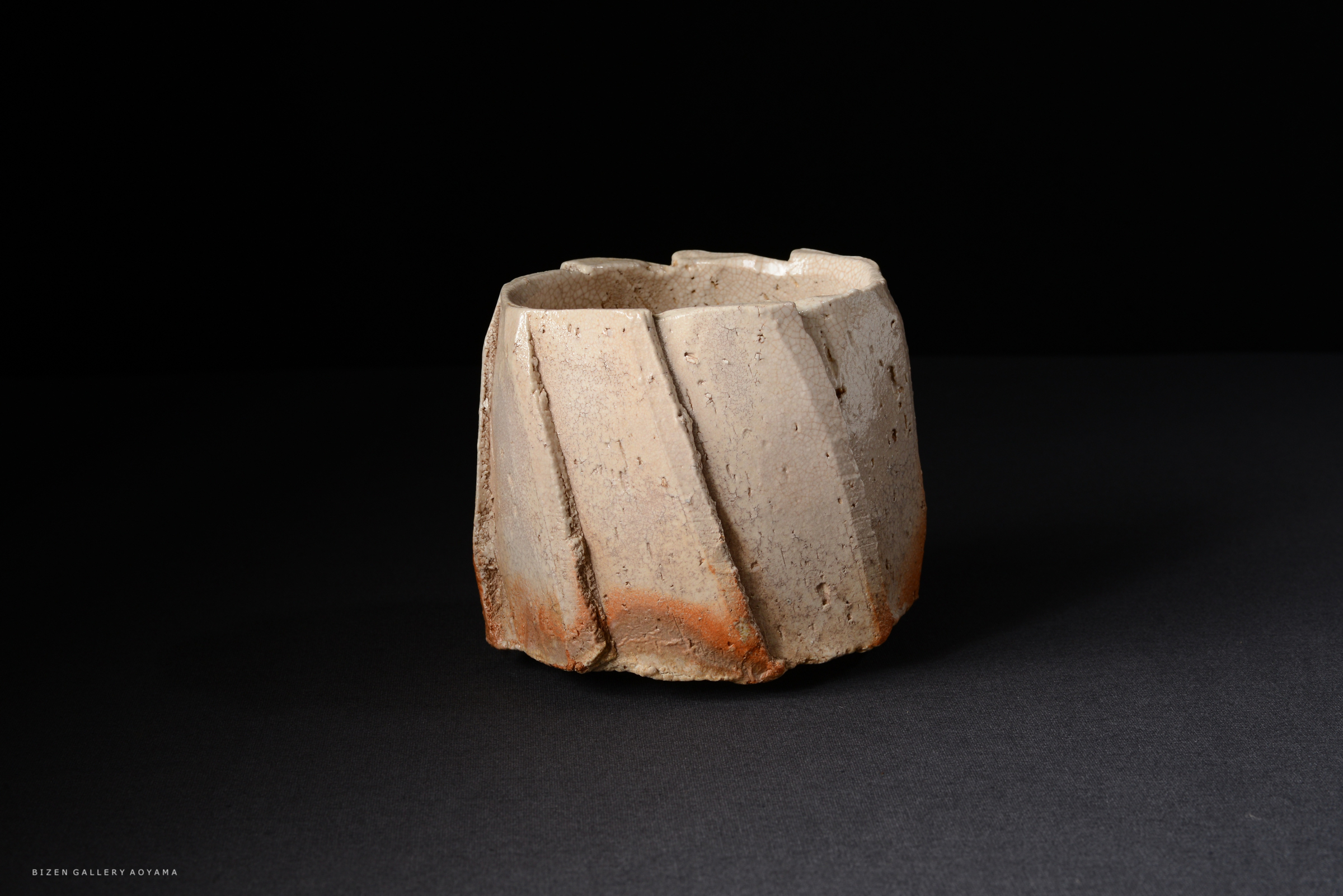 独特な形状の土器の作品。茶色と灰色の質感があり、変わった形の縁を持つ。