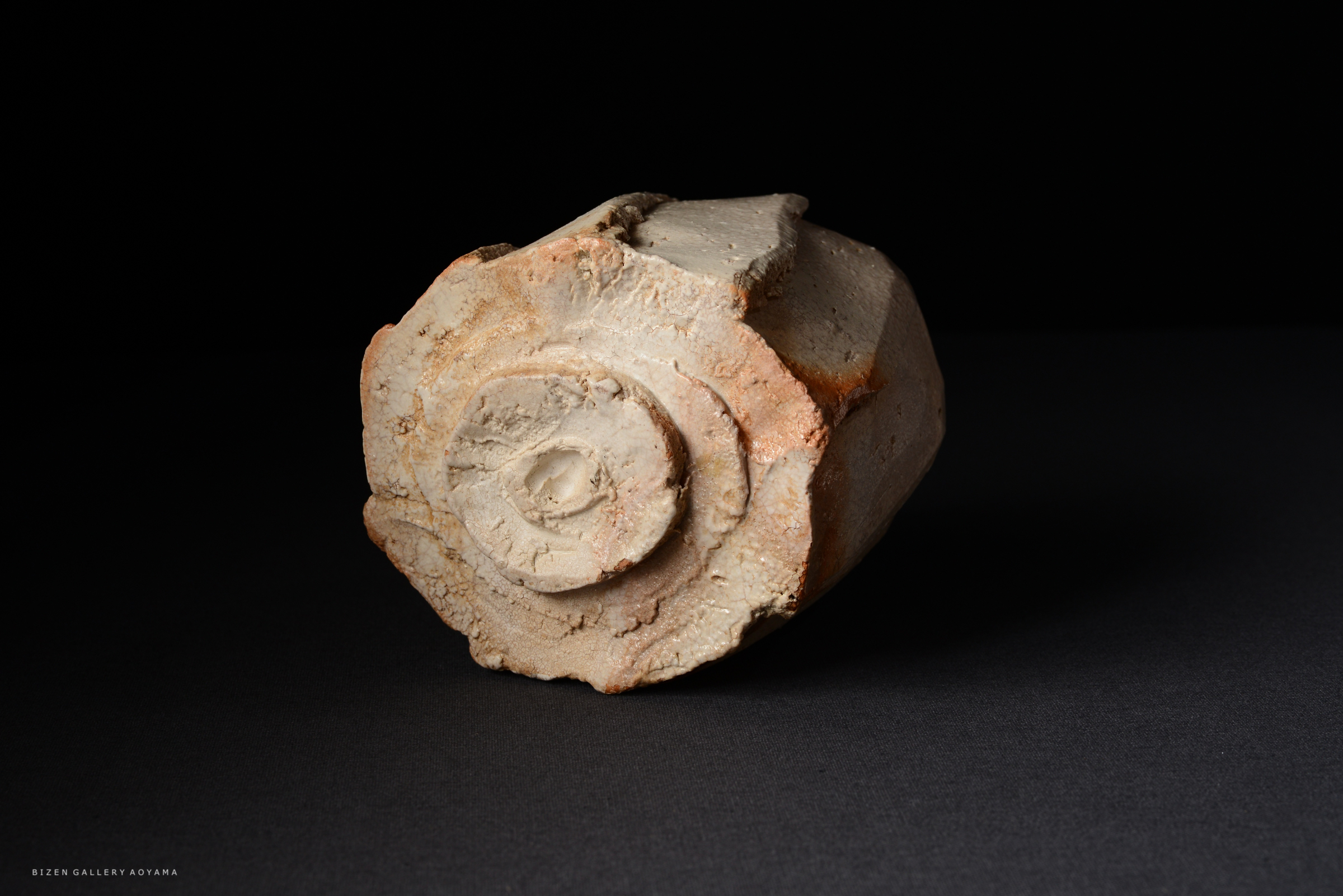 古代の陶器の一部で、滑らかな表面と円形の底面を持つ。暗い背景に置かれた状態で撮影されている。