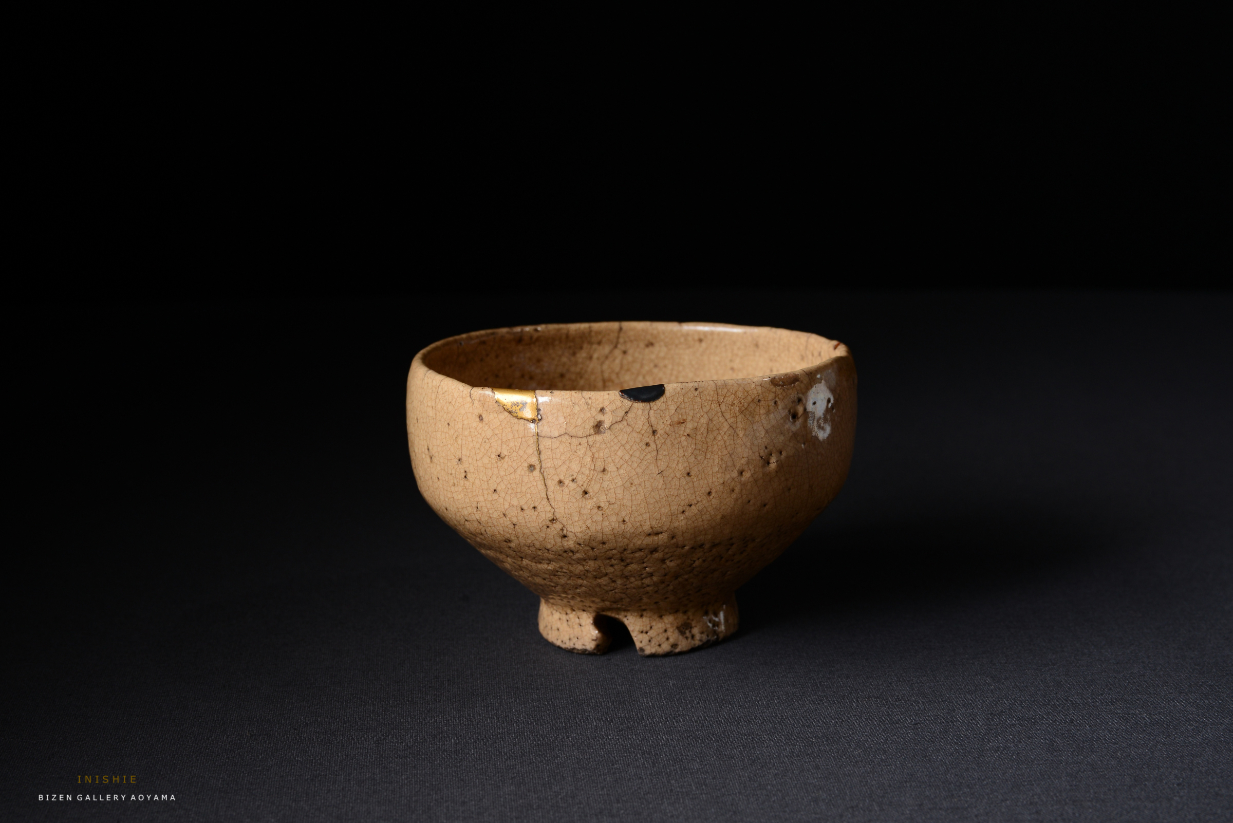 黒い背景の前に置かれた、ひび割れた薄い茶色の陶器の茶碗。