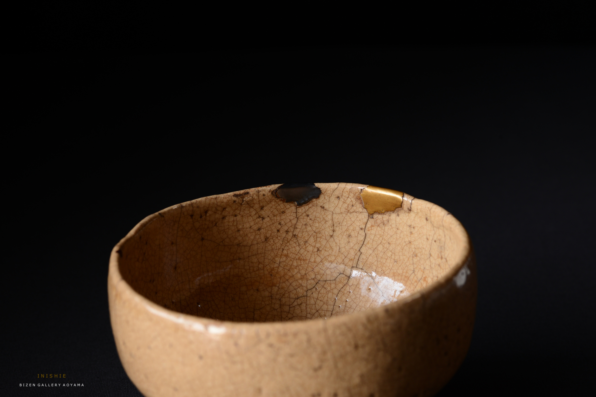 黒い背景に置かれた、ひび割れた陶器の茶碗。部分的に金色と黒色の補修が施されている。