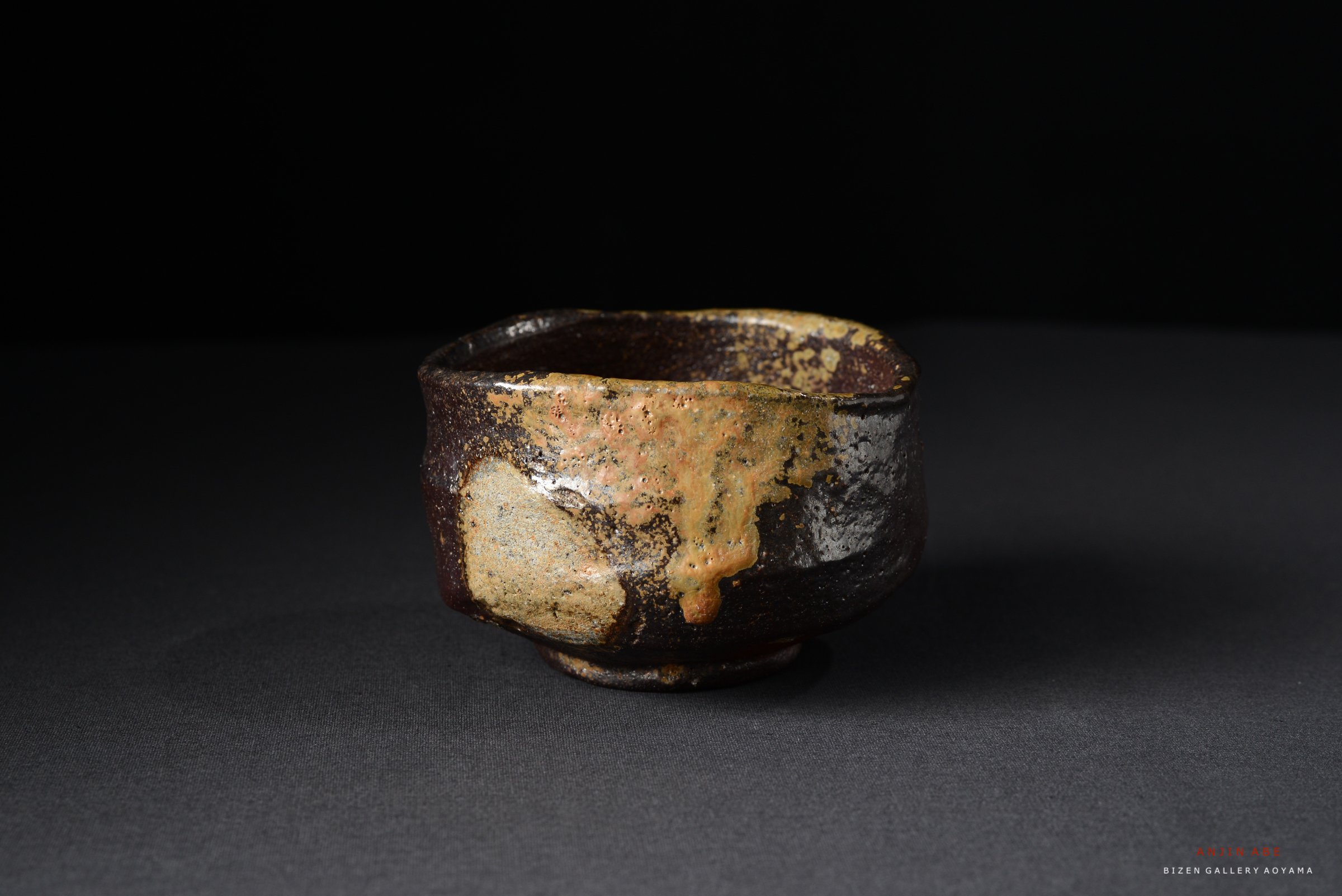 独特の質感と色合いを持つビゼン焼きの陶器の茶碗。黒い背景に対して、茶碗の表面の模様が際立っている。