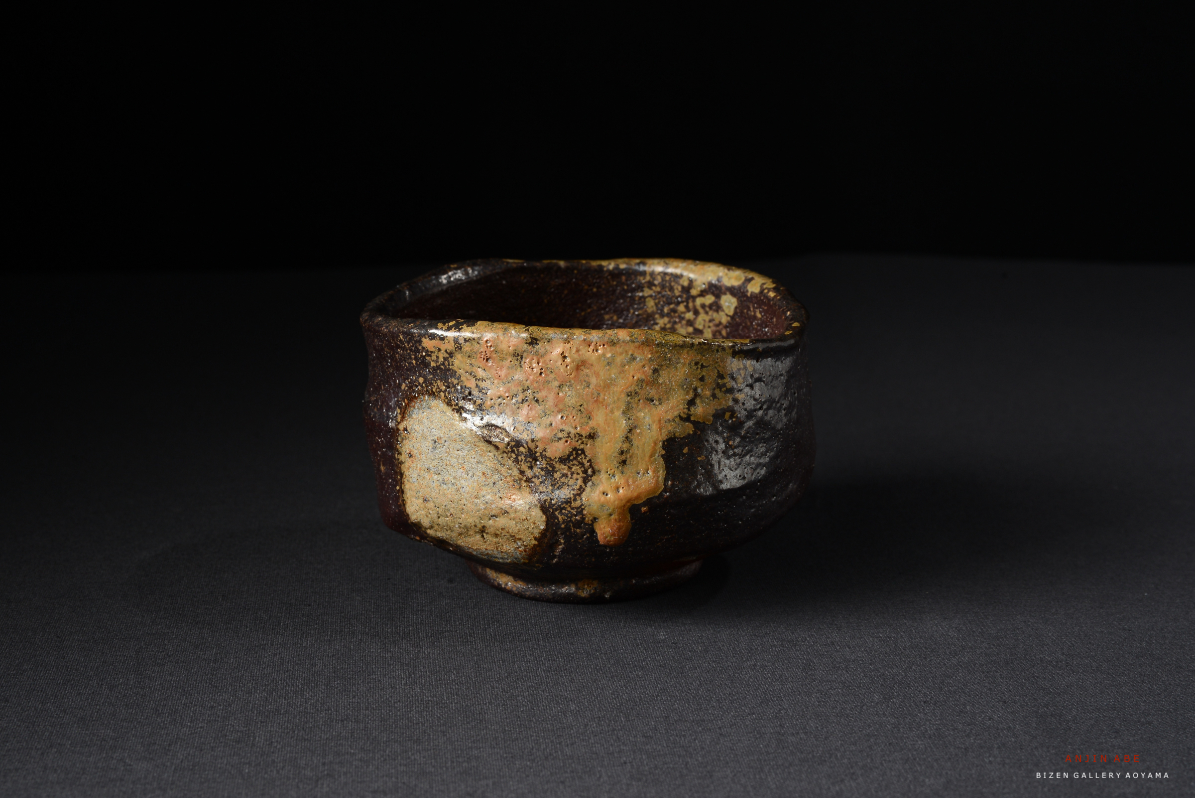 黒い背景の前に置かれた、独特の釉薬の模様を持つ陶器の茶碗