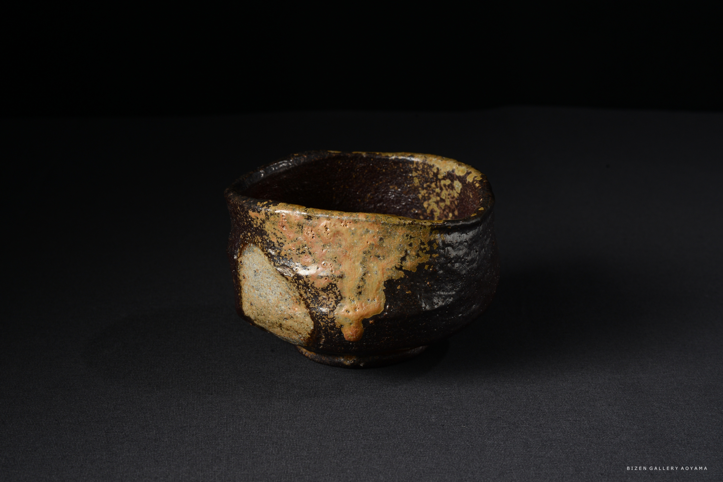 黒い背景の上に置かれた、独特の釉薬が施された陶器の茶碗。表面には茶色とオレンジの斑点が見られる。