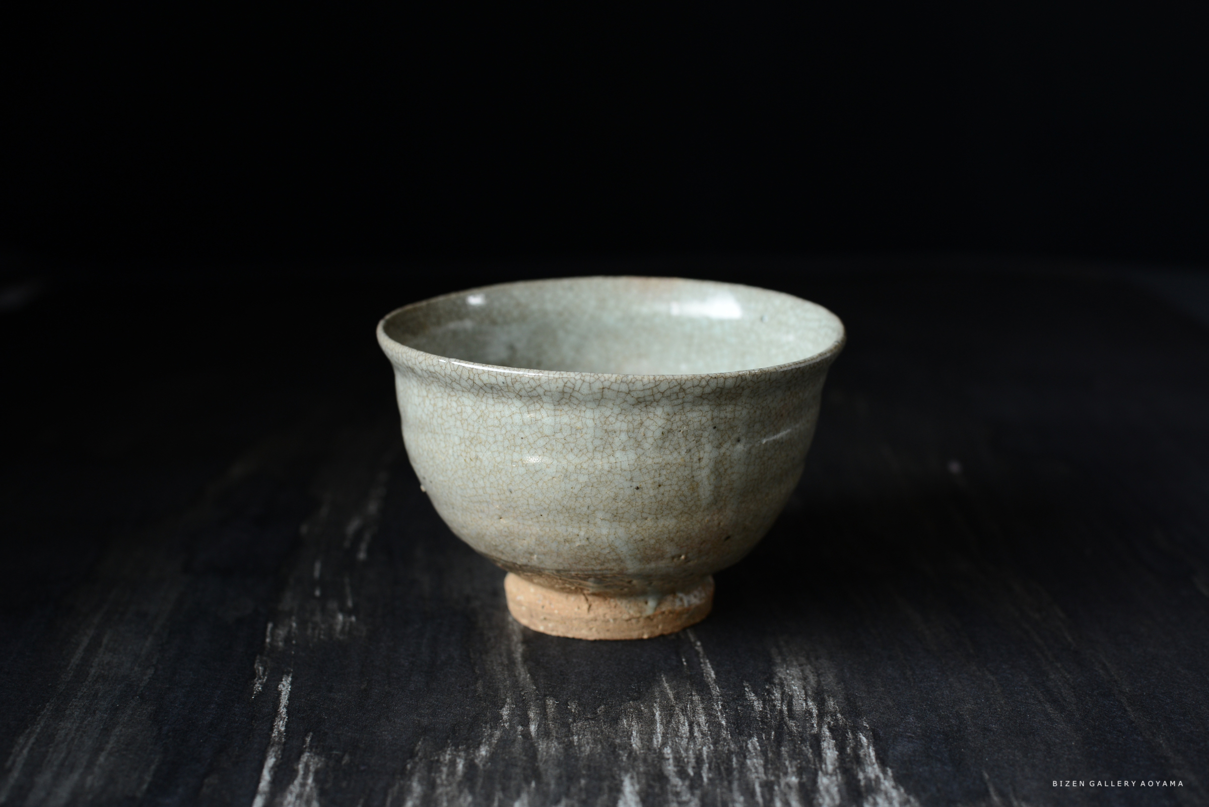 黒い背景の上に置かれた、ひび割れた表面を持つ灰色の茶碗