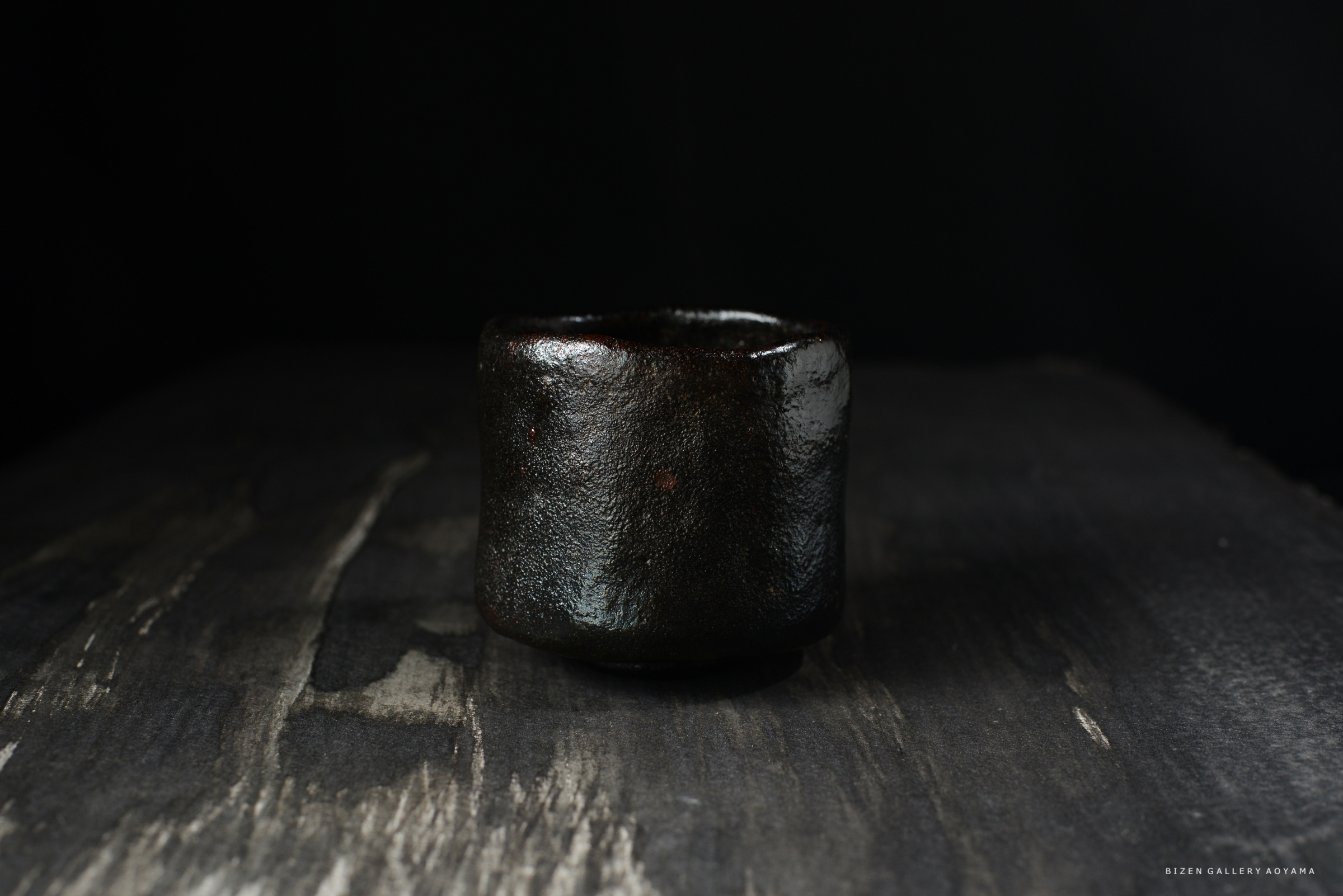 黒い陶器の器が暗い背景で際立っています。木のテーブルの上に置かれています。