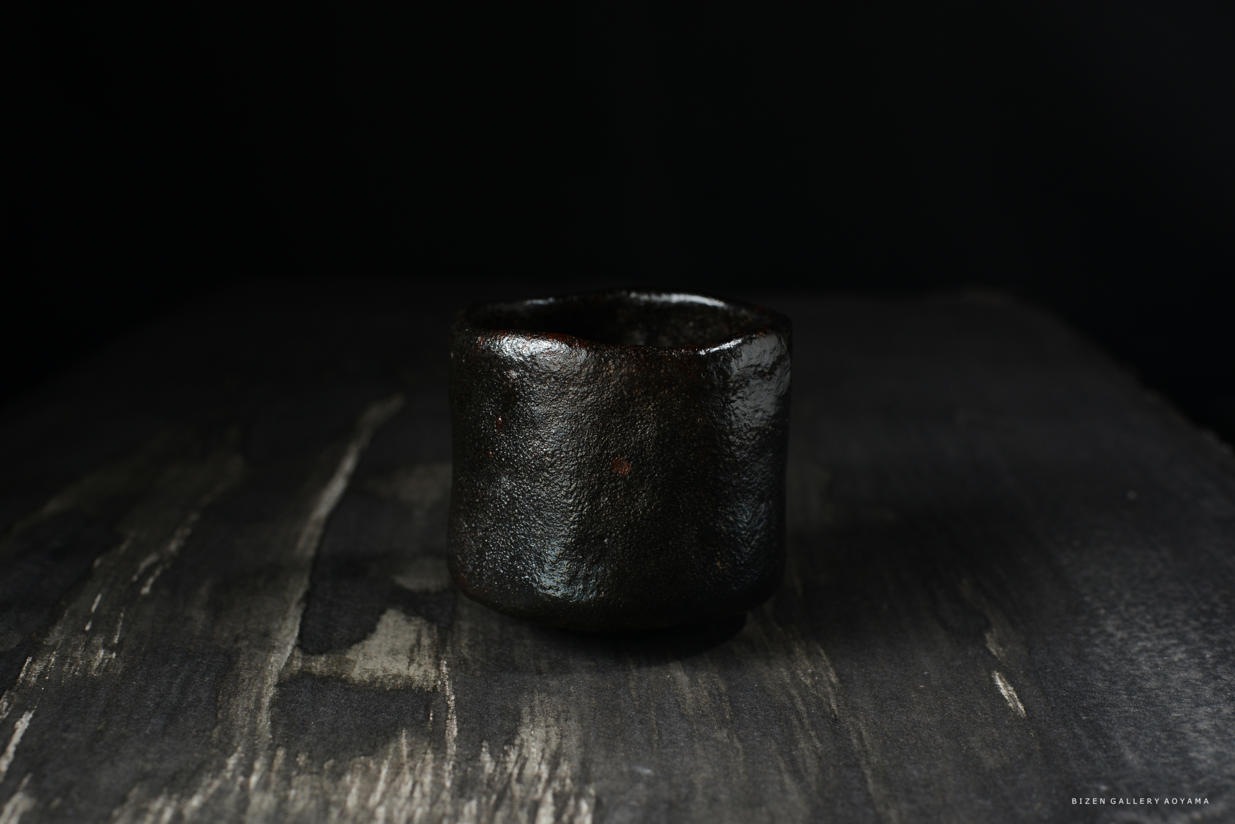 黒い陶器の茶碗が、暗い背景と木製のテーブルの上に静かに置かれています。