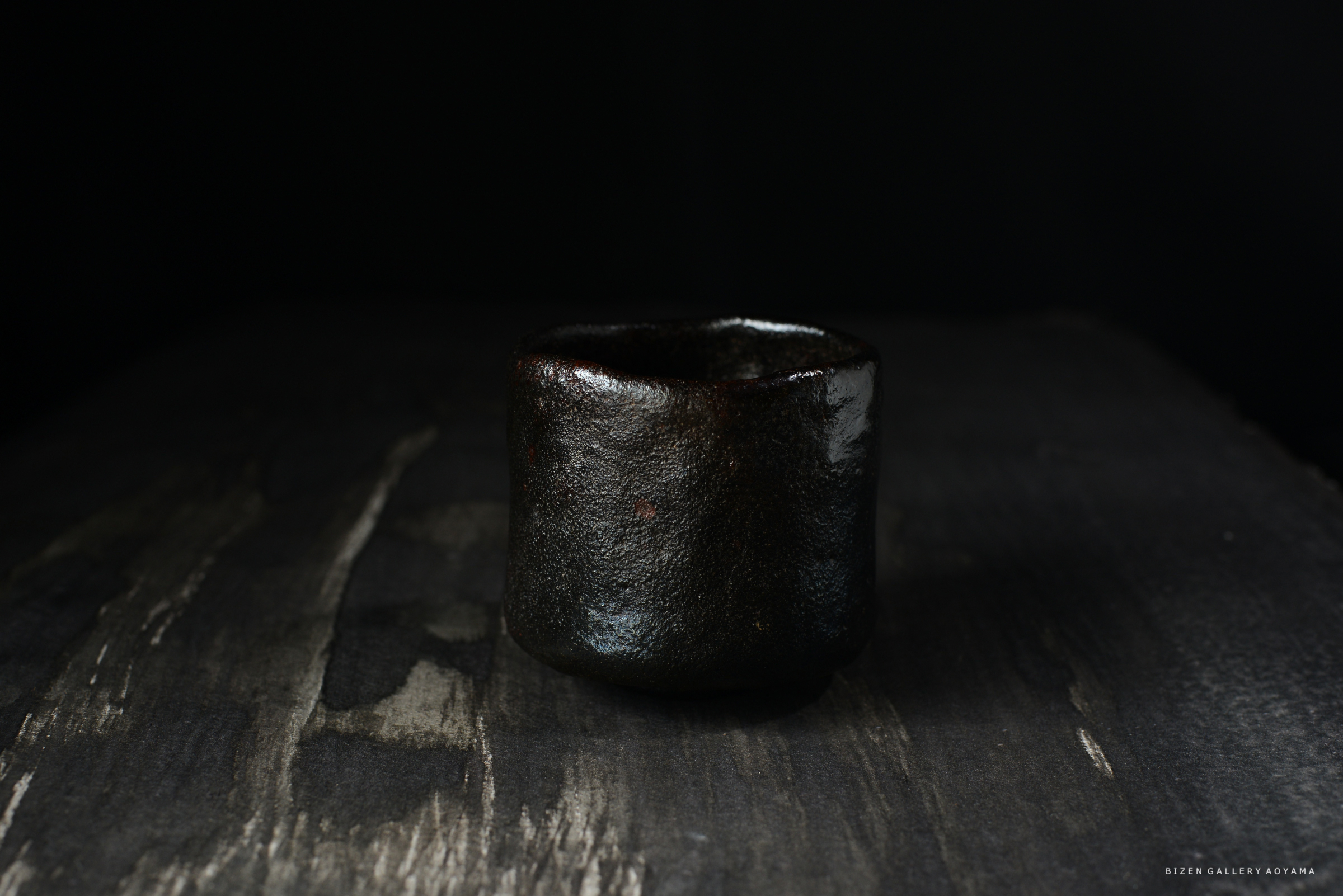 黒い陶器の茶碗が、暗い背景の上に置かれている
