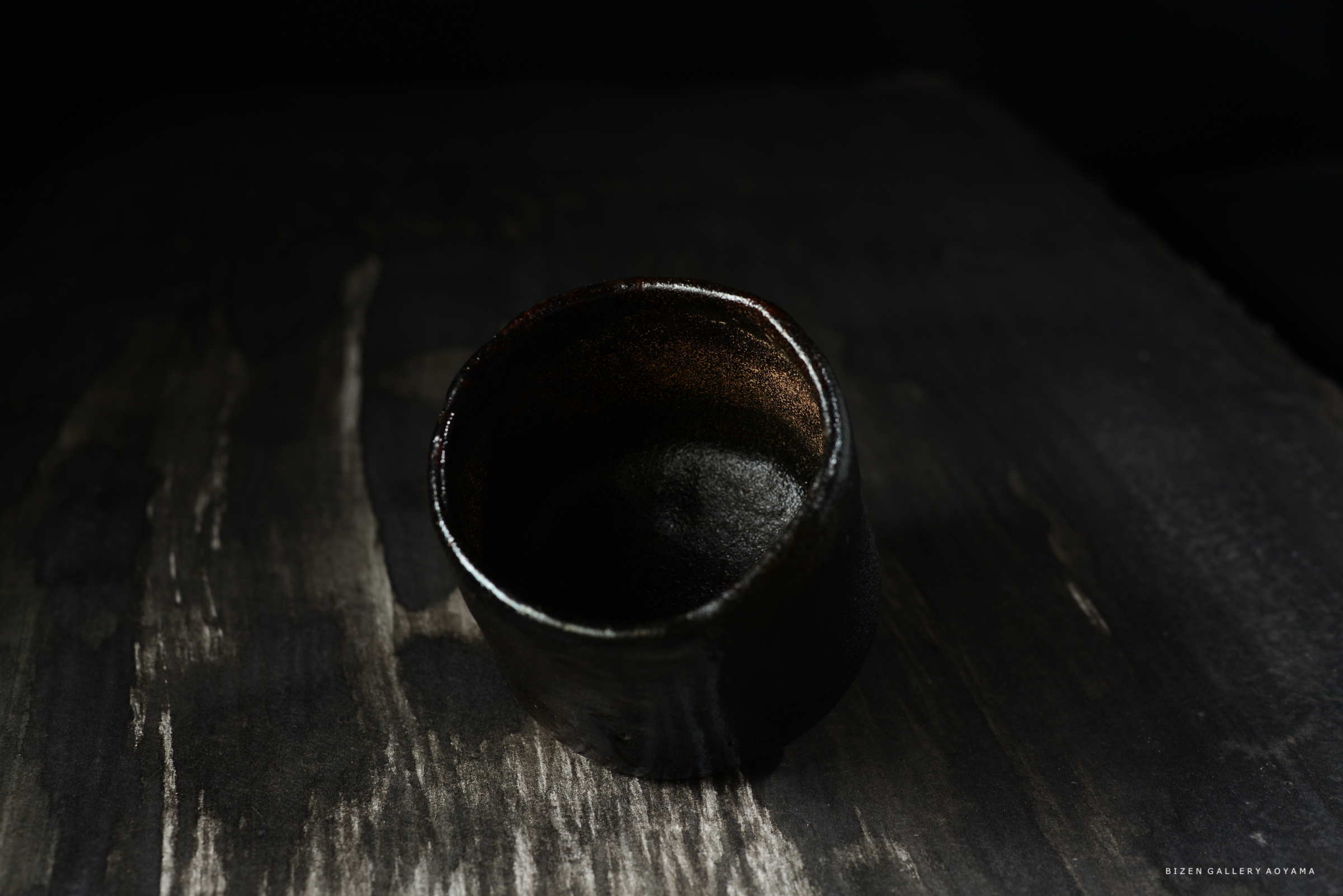 黒い背景の上に置かれた、艶のある黒色の陶器の茶碗。