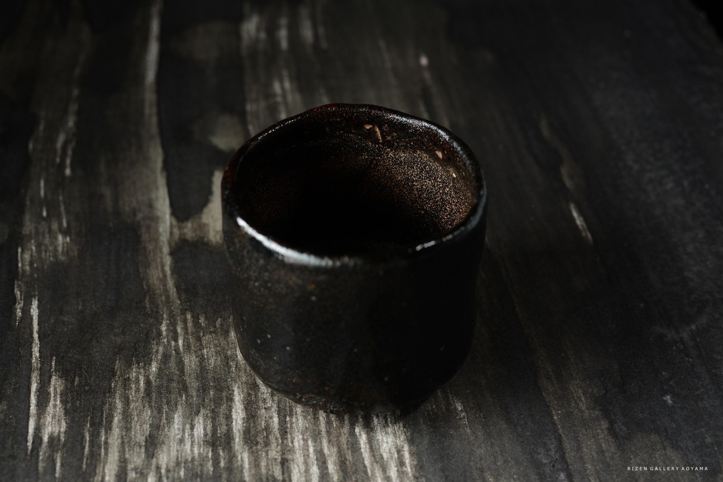 黒い陶器の湯飲みが木の台の上に置かれている