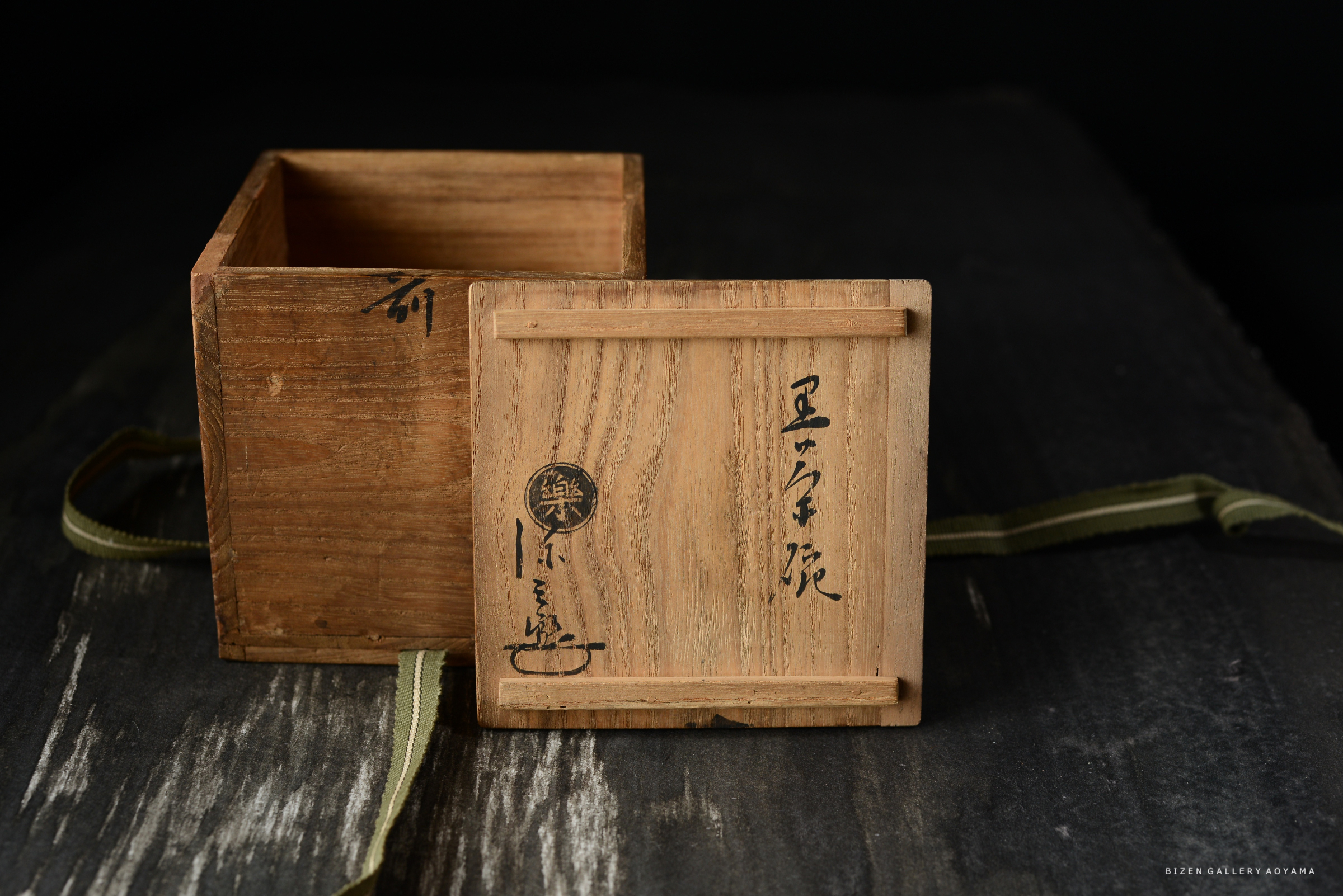 木製の箱が開いている状態で、表面に漢字の書かれた文字があります。箱はシンプルで、黒い背景に置かれています。