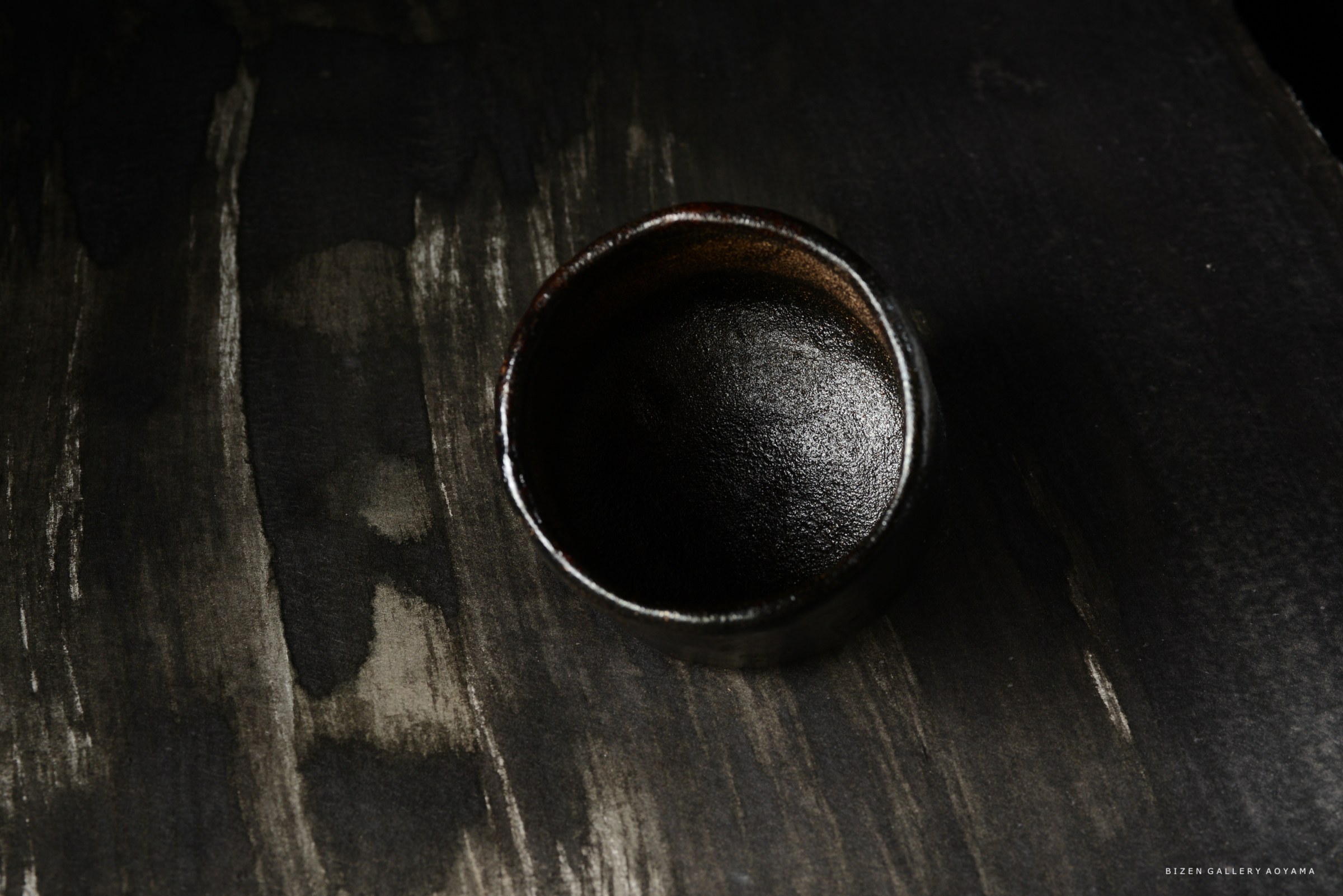 黒い釉薬の陶器の碗が、暗い背景の上に置かれている画像