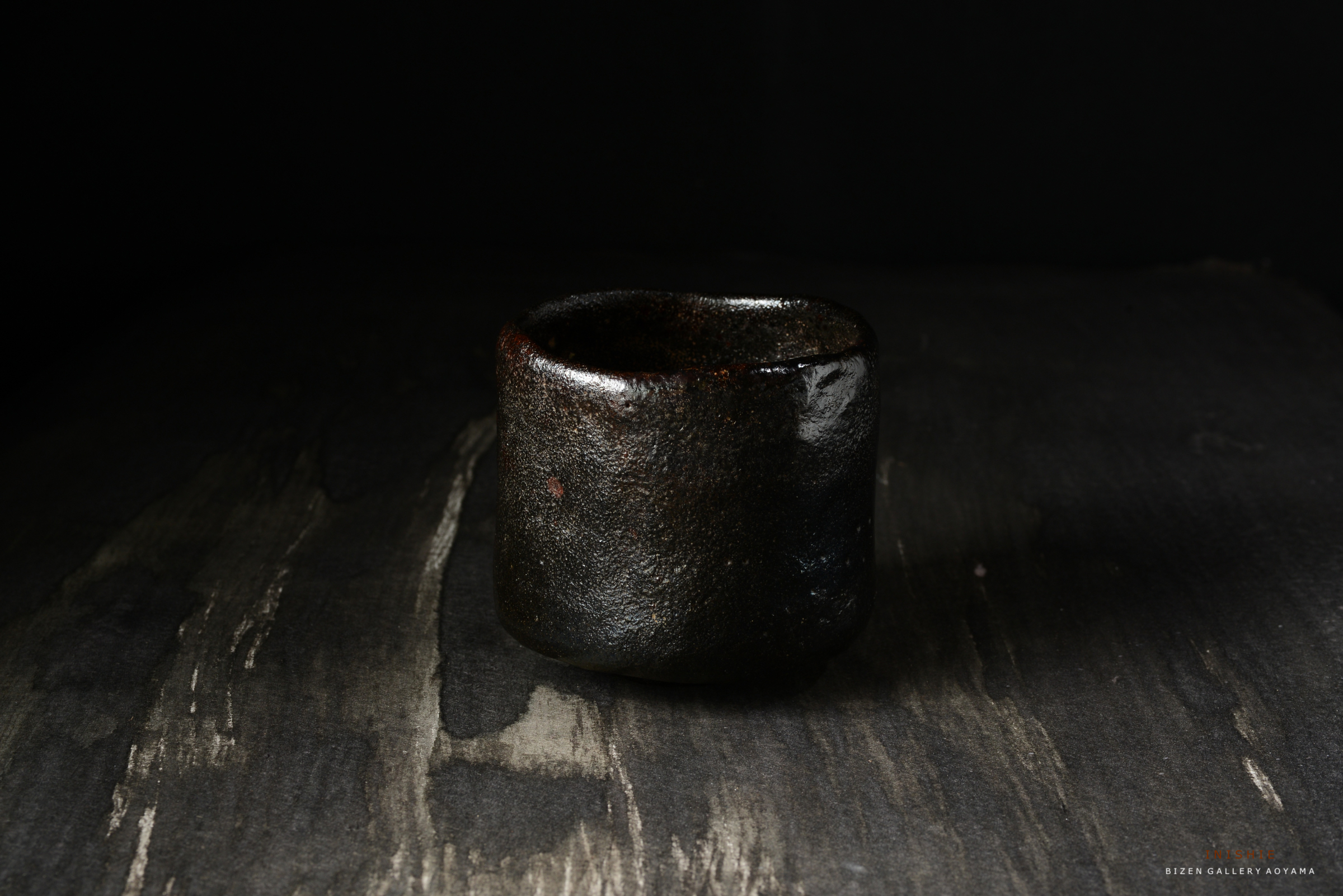 黒い陶器の杯が木のテーブルの上に置かれている画像