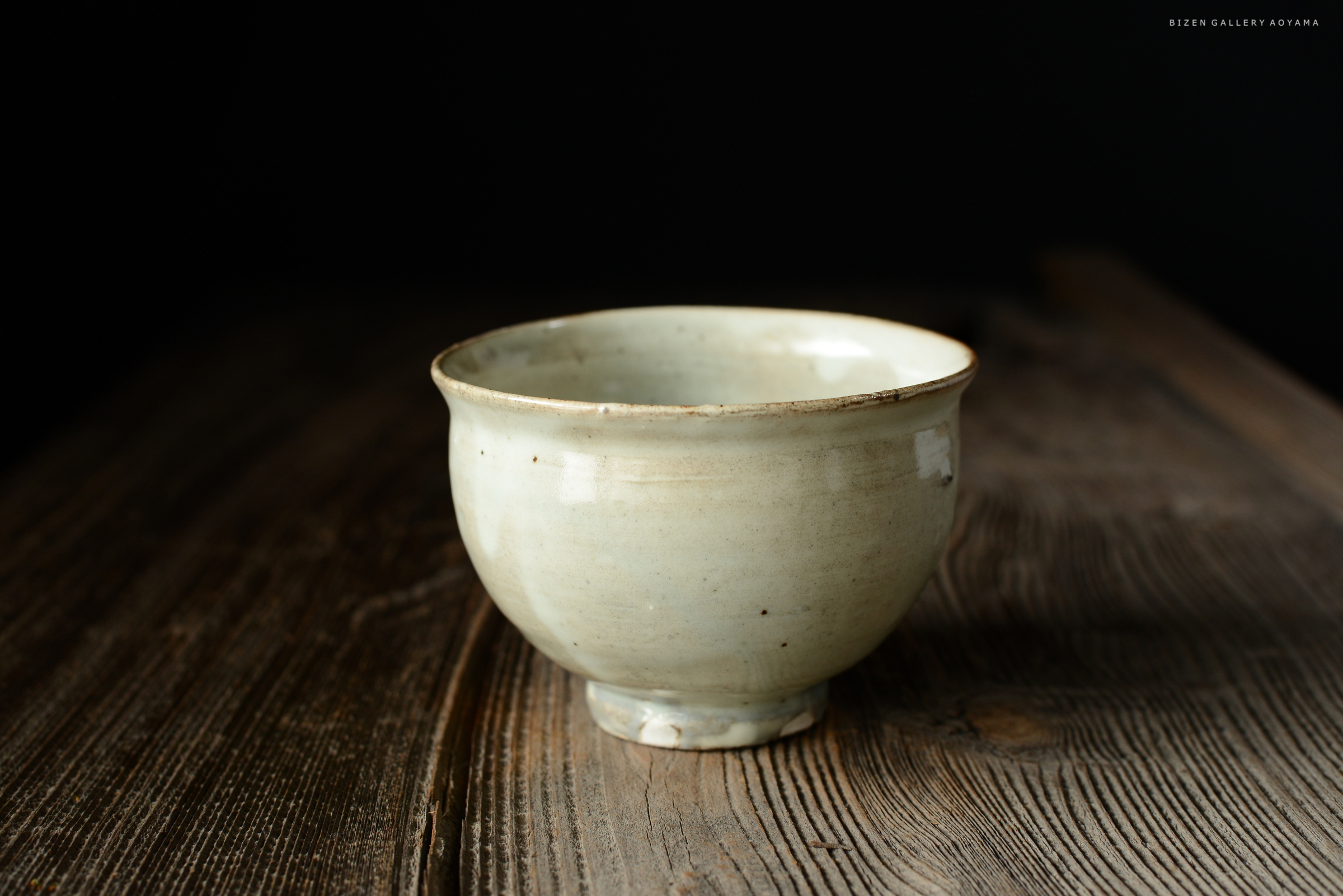 茶碗の上面にフォーカスした、美しい緑がかった色合いの陶器の茶碗。木のテーブルに置かれ、背景は黒でシンプルに演出。