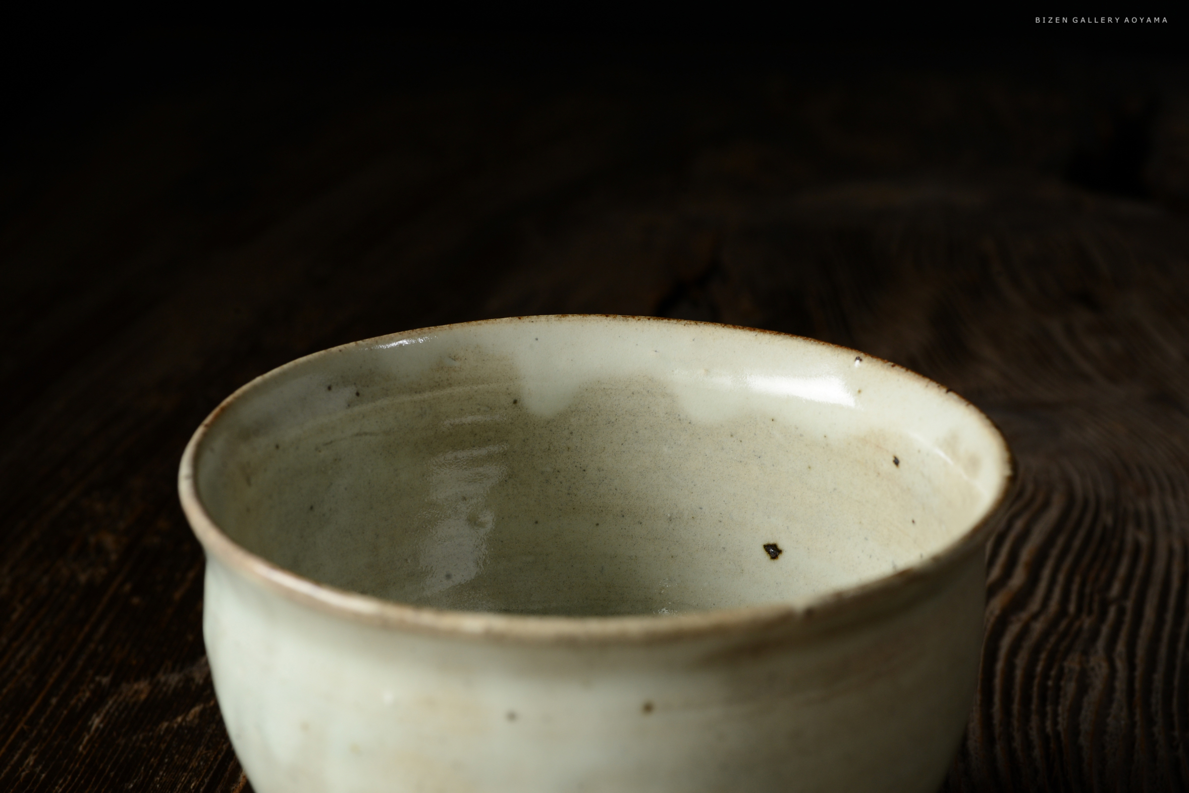 茶碗のクローズアップ。白い釉薬が施された陶器で、内側に細かな模様が見える。背景は暗い木製のテーブル。