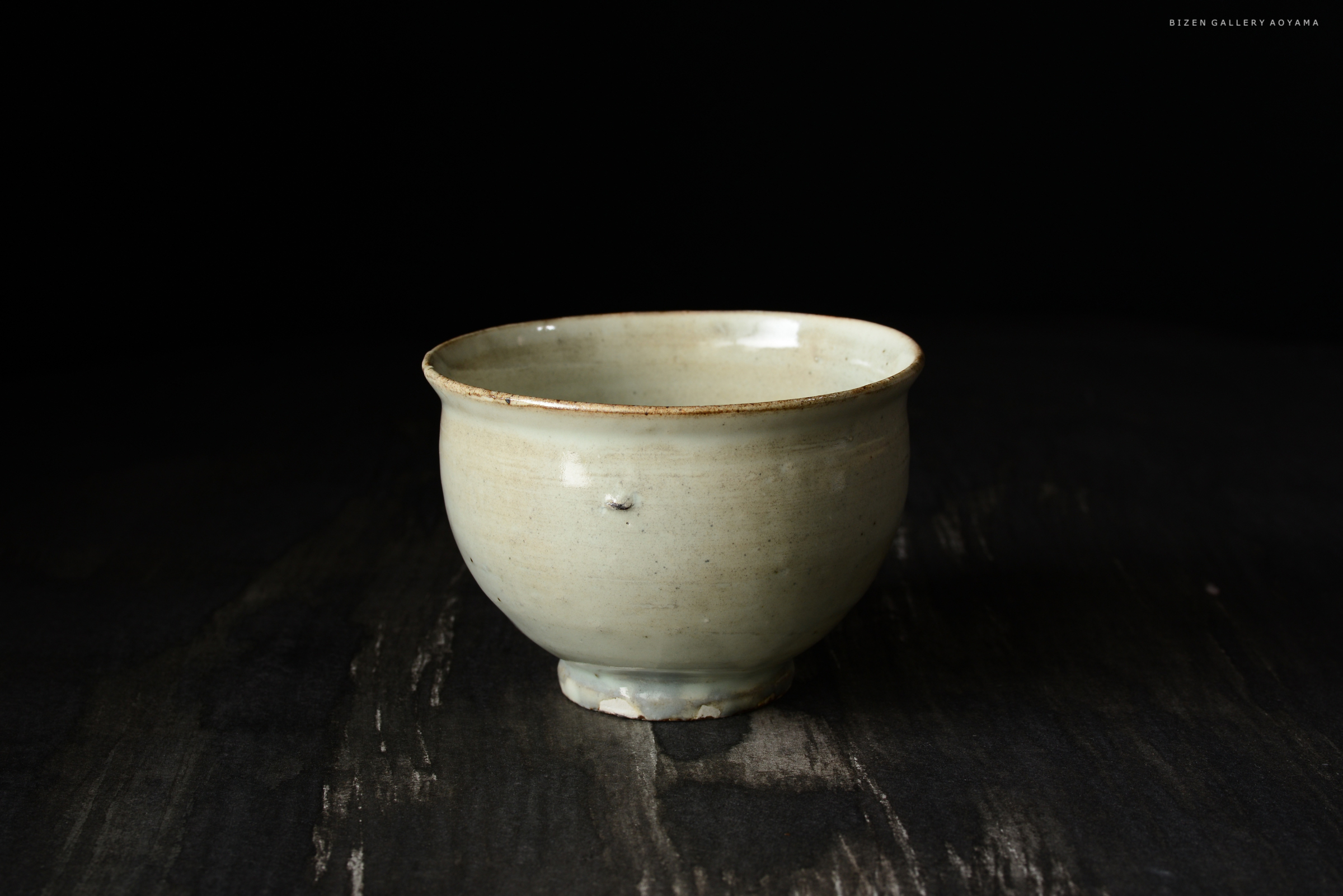 軽やかな陶器の茶碗、柔らかな緑色が特徴で、シンプルなデザイン。暗い背景に対して際立っている。