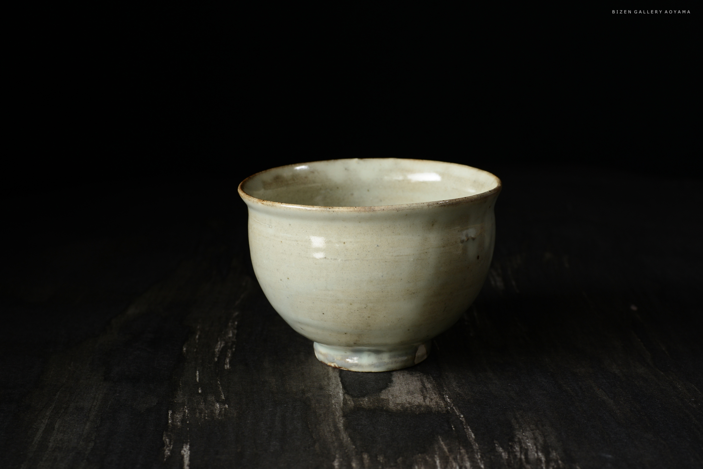 黒い背景に置かれた、淡い色合いの陶器の茶碗