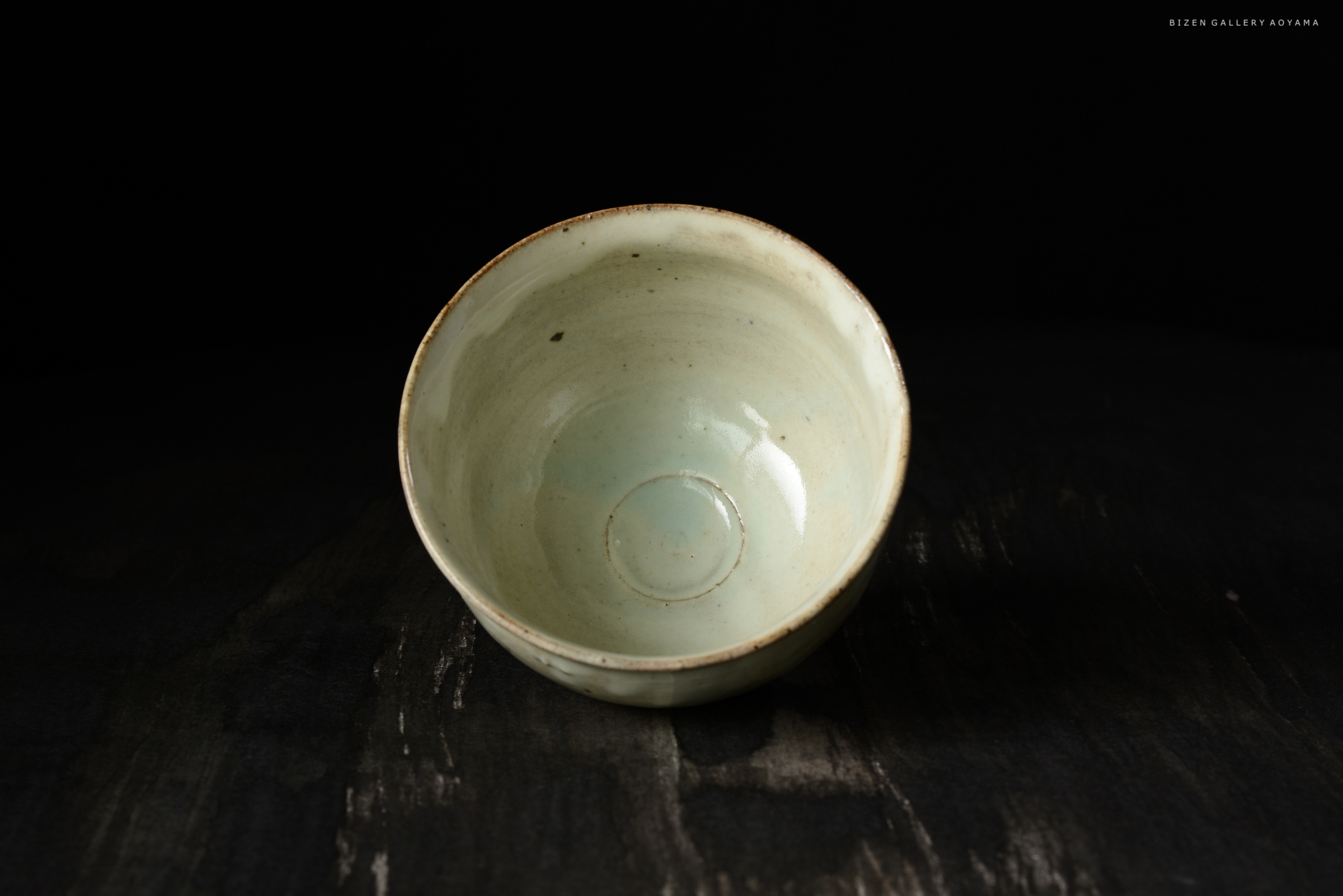 黒い背景に置かれた淡い緑色の陶器の碗