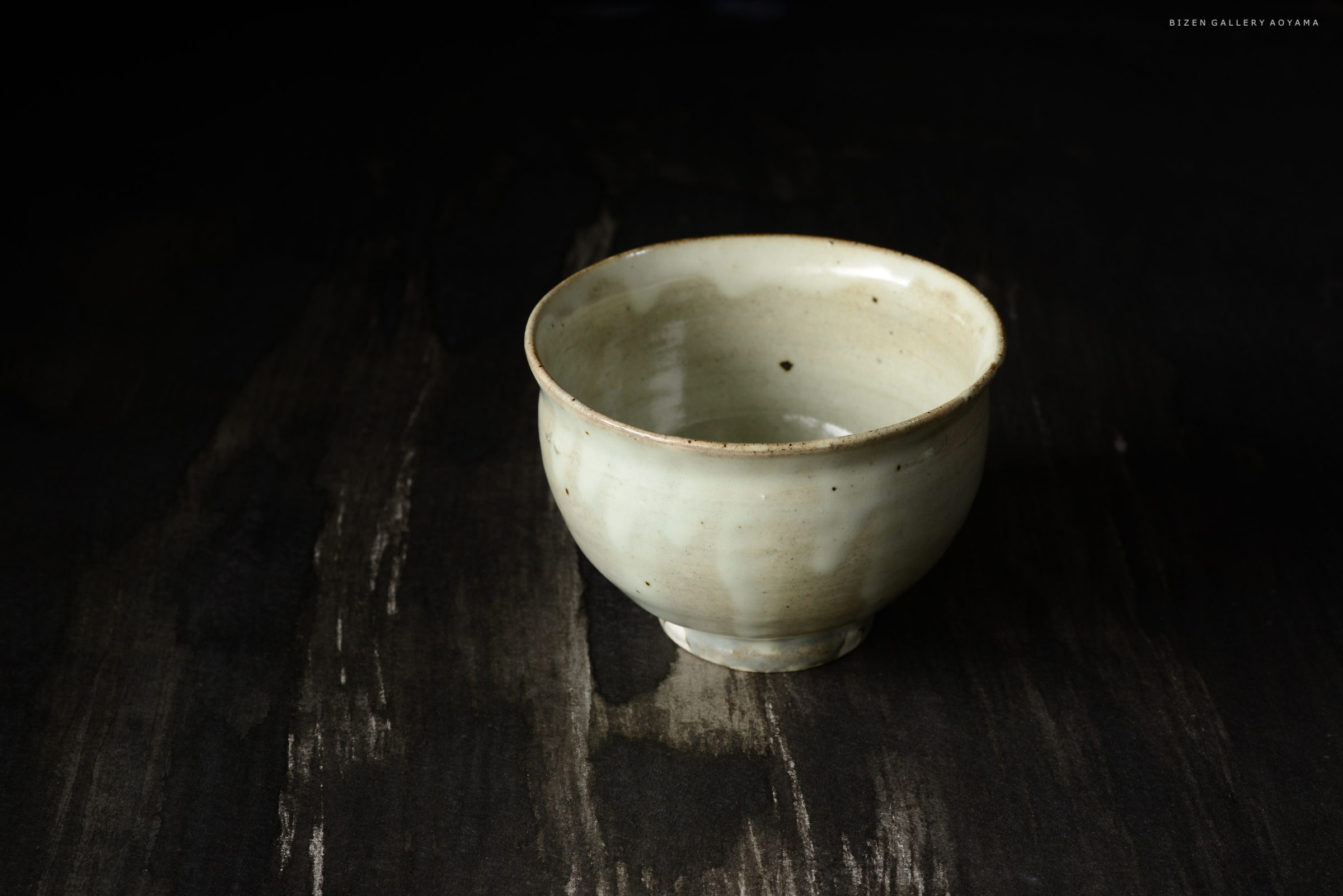 黒い背景の上に置かれた、淡い色合いの陶器の茶碗