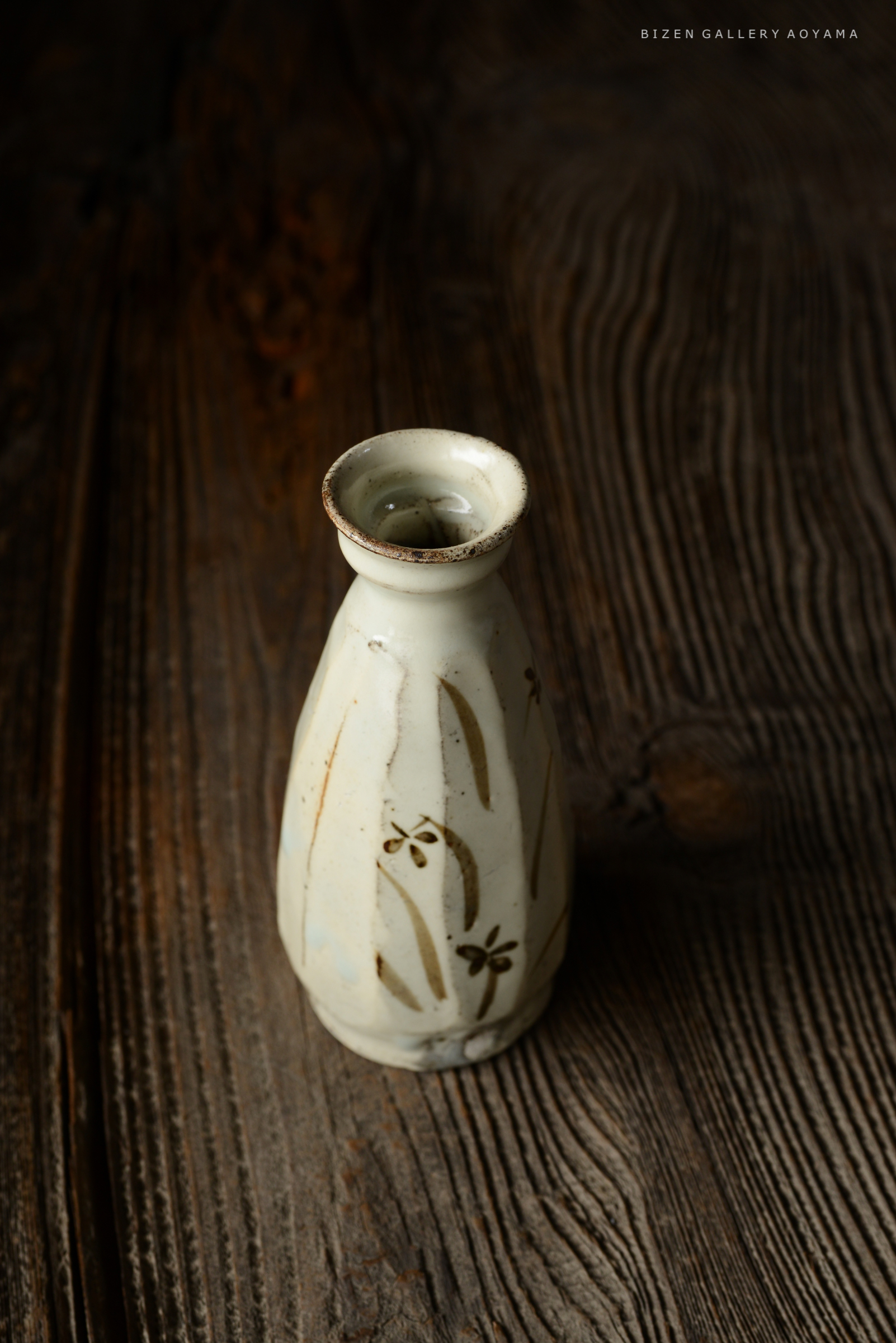 手彫りの模様が描かれた白い陶器の花瓶が、木製のテーブルの上に置かれている