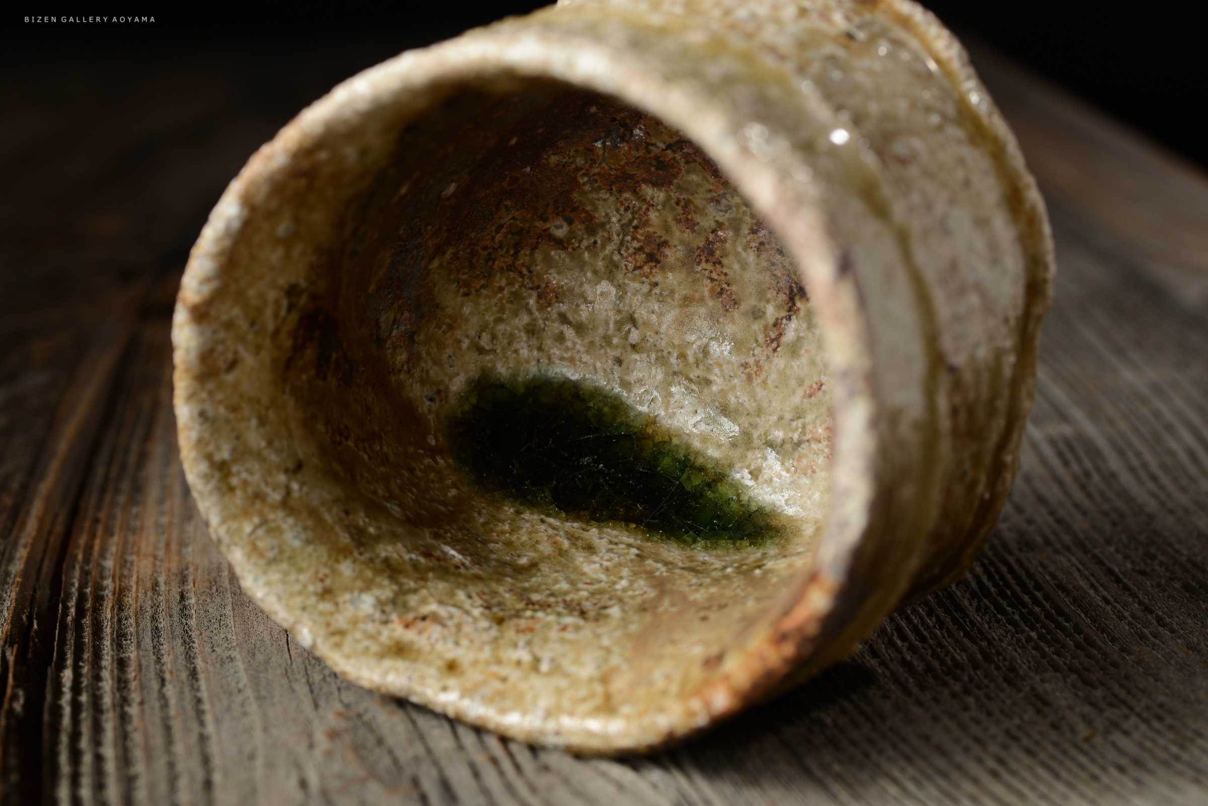内側が緑色の釉薬で仕上げられた陶器の器。木のテーブルの上に配置されている。